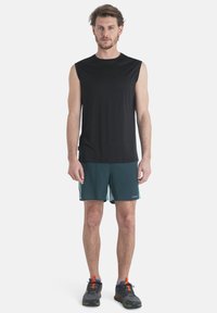 Svart ärmlös träningströja i kombination med turkosa shorts, som har dragsko i midjan, och grå sportskor med orangea detaljer.