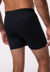 Schwarze Baumwollboxershorts mit einem elastischen Bund, glatter Textur und einem eng anliegenden Design, das bis zur Mitte des Oberschenkels reicht.