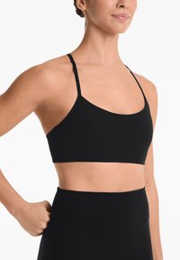Zwarte sport-bh met dunne banden, naadloos ontwerp en rekbaar materiaal, gecombineerd met hoge zwarte leggings. Soepele textuur en minimale accenten.