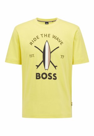 Gelbes Baumwoll-T-Shirt mit einem grafischen Design, das ein Surfbrett und gekreuzte Paddel zeigt. Der Text lautet "RIDE THE WAVE" und "BOSS." Kurze Ärmel.