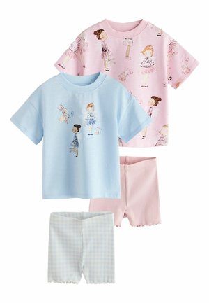 Két mosolygó kisgyermek kézen fogva, nyomott mintás pasztell pólókat, rövidnadrágot és tornacipőt viselve, sima bézs háttér előtt áll.