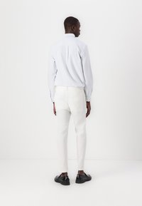 Chemise à rayures bleu clair avec un pli au dos, associée à un pantalon blanc et des chaussures en cuir noir, vue de dos.