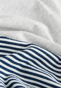 Textilie mají světle šedou hladkou tkaninu vrstvenou s bílým a námořnickým pruhovaným bavlněným vzorem, který ukazuje různé textury a vzory.