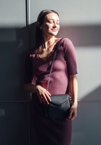 Černá kožená kabelka s řetízkovým popruhem, s strukturovaným designem a ostrým klopem. Modelka má na sobě proužkované šaty v barvě švestek.