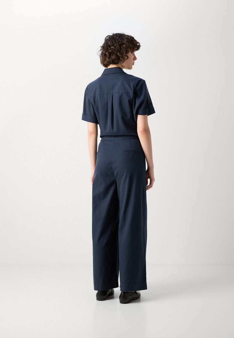 Navyblauer Jumpsuit mit kurzen Ärmeln, lockerer Passform und weitem Bein. Verfügt über einen kragenförmigen Ausschnitt und Seitentaschen. Glatte Stofftextur.