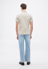 Ανοιχτό γκρι πόλο μπλουζάκι με κοντά μανίκια, συνδυασμένο με ψηλόμεσα, φαρδιά ανοιχτό μπλε τζιν παντελόνια και μαύρα παπούτσια. Απλός σχεδιασμός και απαλό ύφασμα.