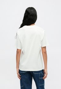 Biela bavlnená tričko s uvoľneným strihom, okrúhlym výstrihom, krátkymi rukávmi a bez viditeľnej grafiky. Nosené s modrými cargo nohavicami.