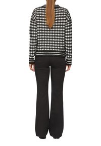 Zwart-wit geblokte gebreide cardigan met geribbelde zoom, gecombineerd met zwarte flared broek. De stof lijkt textuur te hebben met contrasterende kleuren.