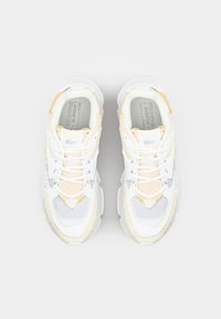 Baskets blanches épaisses avec des accents pêche clair et gris, panneaux en mesh, superpositions texturées et système de laçage à l'avant. Logo Lacoste sur la languette.