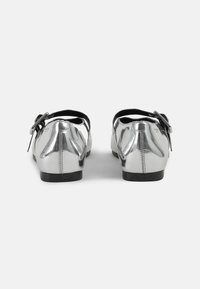 Silver metallic ballet flats with a round toe, low black heel, and a decorative black strap with buckle detail on each shoe.