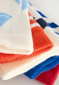 Färgglada stickade strumpor i vitt, blått, orange och rött. Texturerade mönster inkluderar ränder och geometriska former, som visar upp olika färger.