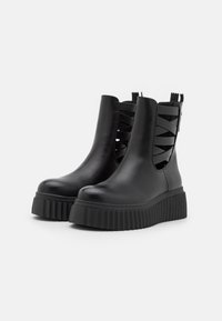 Czarne botki na platformie z cholewką z gładkiej skóry, z wyciętymi detalami po bokach oraz żebrowanymi gumowymi podeszwami zapewniającymi przyczepność i stabilność.
