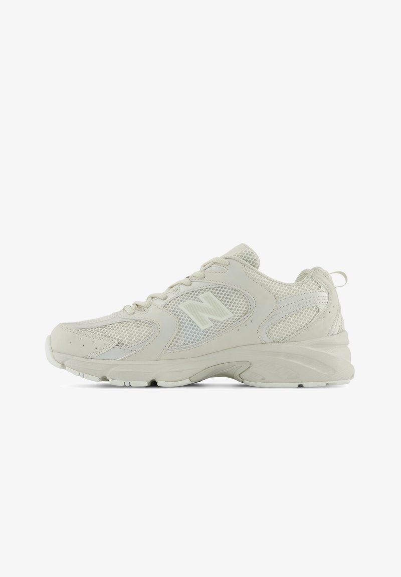 Baskets New Balance beige clair avec panneaux en mesh et cuir, fermeture à lacets, semelle rembourrée et logo "N" de marque sur le côté.