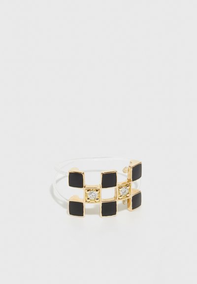 Gold-tone ring featuring black enamel squares and two clear stones, with an open, flexible band design. Smooth texture, modern geometric pattern.