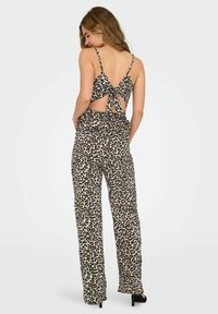 Jumpsuit in stampa leopardata con spalline sottili, schiena aperta con dettaglio annodato e pantaloni a gamba larga. Il materiale sembra leggero e testurizzato.
