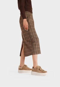 Maglione lavorato a maglia marrone, gonna midi a quadri con spacco laterale e sneakers beige con lacci, suola platform e dettagli in argento.