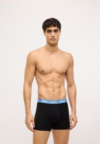 Boxer briefs neri con un elastico blu chiaro che presenta il testo "HUGO". Materiale in cotone morbido, design aderente e lunghezza fino a metà coscia.