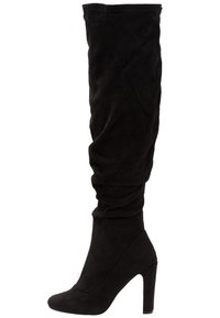 Bota alta de tacón negro, por encima de la rodilla, hecha de suave material de ante. Presenta un diseño holgado y una punta afilada con un tacón robusto.