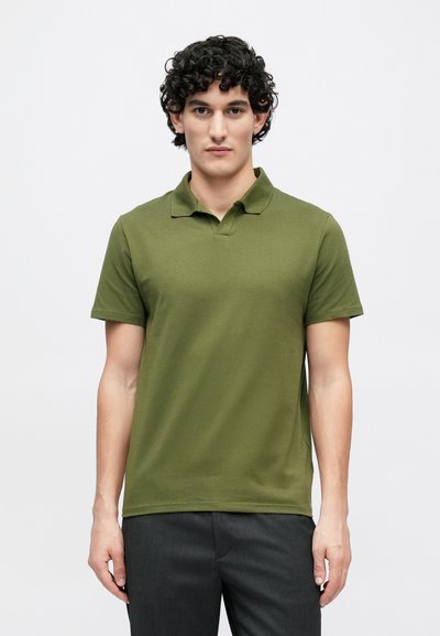 Īsām piedurknēm polo krekls olīvu zaļā krāsā, izgatavots no mīkstas kokvilnas, ar klasisku apkakli un brīvu piegriezumu, kombinēts ar tumši pelēkām biksēm.