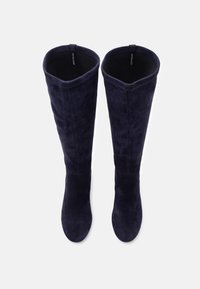 Tengerészeti suéd térdig érő csizmák sima textúrával, enyhén formázott szárakkal és széles nyílásokkal a tetején, minimális fém részletekkel.