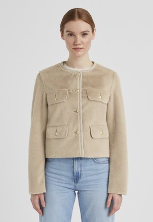 Beige, kurz geschnittene Jacke aus weichem, strukturiertem Stoff. Verfügt über vier Vorderaschen und goldene Knopfverschlüsse, umrandet mit einem metallischen Rand.