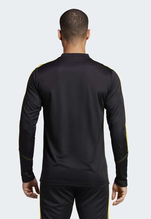 Homme vu de dos portant un haut de sport noir à manches longues avec des bandes jaunes le long des manches et un pantalon noir assorti.