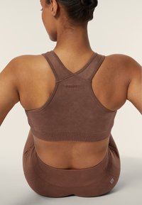 Reggiseno sportivo marrone con texture a coste e design incrociato, con il nome del marchio "FREDDY" in evidenza sulla schiena.