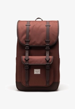 Zaino in tessuto marrone con spallacci e fibbie in pelle scura, tasca frontale e etichetta del marchio Herschel su sfondo bianco.