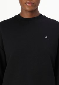 Felpa nera in misto cotone, con scollatura rotonda, maniche lunghe e un piccolo logo bianco "ck" sul lato sinistro del petto.