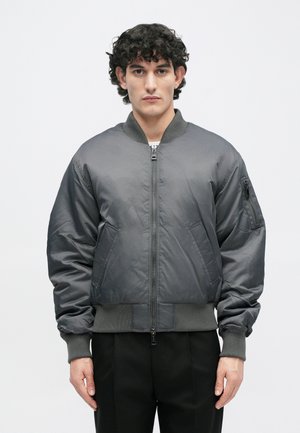 Γκρι αεροπορικό μπουφάν φτιαγμένο από λείο ύφασμα, με μπροστινό φερμουάρ, ριμπ μανσέτες και τσέπη με φερμουάρ στον αριστερό βραχίωνα.