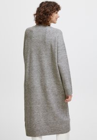 Cárdigan largo de punto gris hecho de una tela suave, con un ajuste relajado, puños acanalados y aberturas laterales. Diseñado con un cuello alto y sin cierres.