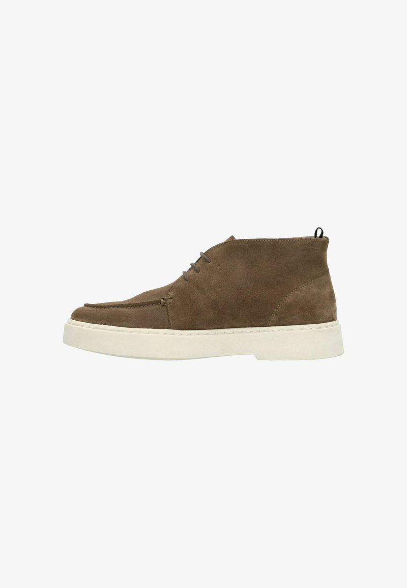Bruine suède high-top schoen met een witte rubberen zool, ronde neus, minimale stiksels en een lus aan de achterkant voor gemakkelijk aan- en uittrekken.