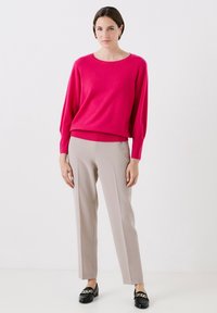 Maglione rosa oversize con scollo rotondo, abbinato a pantaloni beige su misura e mocassini neri con dettaglio a catena.