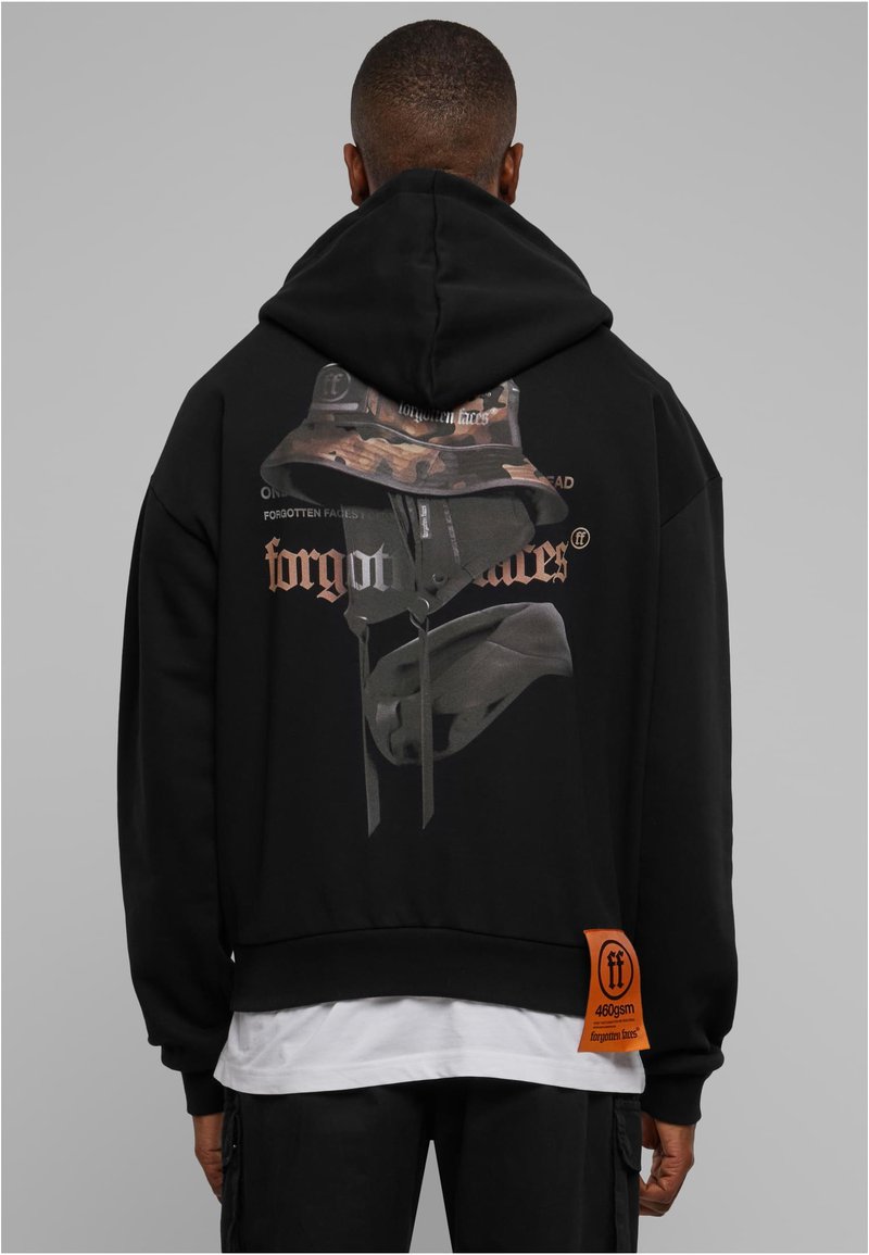 Sudadera negra corta con capucha y un estampado gráfico de un sombrero estilo pescador camuflado y texto "rostros olvidados" en la parte trasera. Cuenta con una etiqueta de tela naranja.