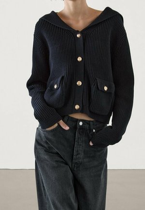 Un cardigan tricoté bleu marine foncé avec capuche, boutons dorés et deux poches avant. Le design présente une texture côtelée et une coupe courte.