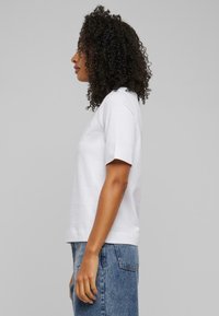 Hvit, bomulls T-skjorte med avslappet passform, korte ermer og rund hals, kombinert med lyseblå denimjeans. Glatt tekstur, minimalistisk design.