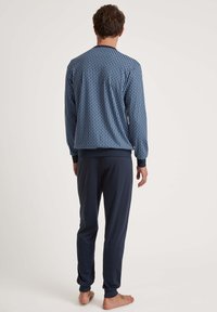 Marine pyjama set met een lange mouwen top met een geometrisch patroon en ribgebreide manchetten, gecombineerd met effen marineblauwe broek met elastische enkels.