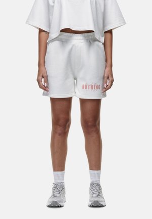 Shorts en mélange de coton blanc avec une taille élastique, arborant un logo rose sur la jambe gauche. Le tissu a une texture lisse.