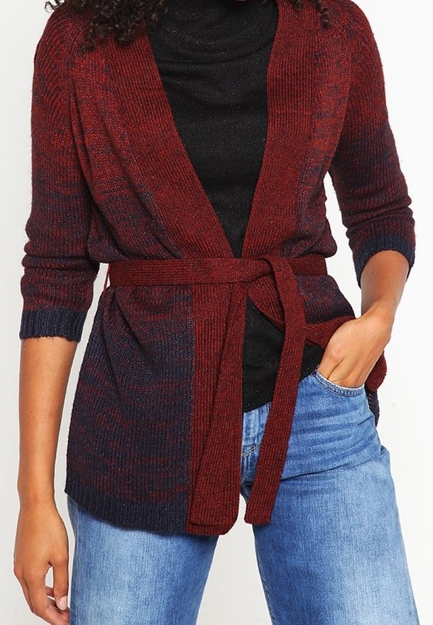 Femme portant un cardigan en maille bordeaux et marine avec une ceinture nouée à la taille, par-dessus un haut noir et un jean bleu.