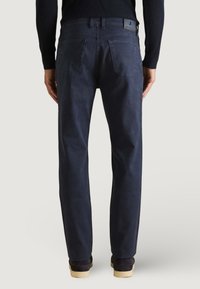 Pantaloni in cotone blu navy con vestibilità dritta, tasche posteriori e etichetta in pelle sulla cintura, abbinati a scarpe scure.
