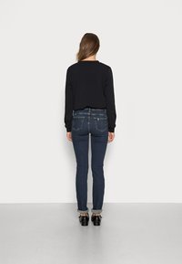 Svart långärmad topp som matchas med mörkblå cigarettejeans. Jeansen har en klassisk femfickdesign och uppvikta muddar. Svarta skor fulländar looken.