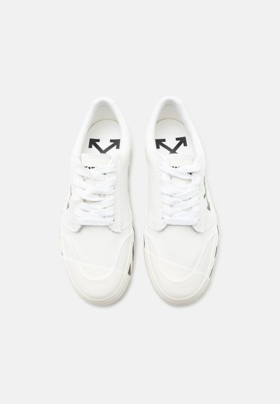 Λευκά παπούτσια χαμηλού προφίλ με λευκά κορδόνια και μαύρο λογότυπο βέλους τυπωμένο στις εσωτερικές σόλες και τις εξωτερικές πλευρές, εμφανιζόμενα από πάνω σε λευκό φόντο.