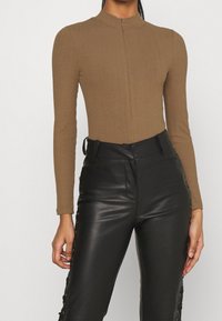 Body con manica lunga marrone a costine con collare alto e zip frontale, abbinato a pantaloni in pelle nera a vita alta con lacci laterali.