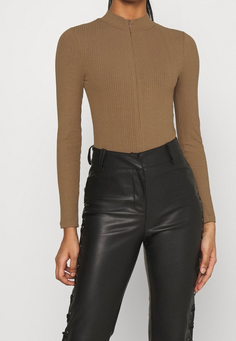 Body con manica lunga marrone a costine con collare alto e zip frontale, abbinato a pantaloni in pelle nera a vita alta con lacci laterali.