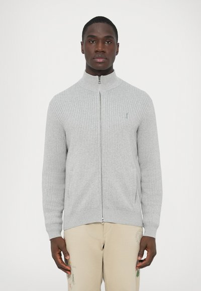Pull gris clair à fermeture éclair avec texture côtelée, col montant, et un petit logo brodé sur la poitrine. Comprend des poches latérales.