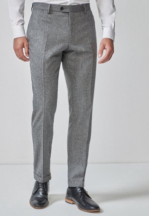 Grau karierte Hose im Slim-Fit-Design mit Gürtelschlaufenbund, Seitentaschen und Bündchen, kombiniert mit schwarzen Schnürschuhen.