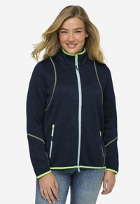 Giacca navy a zip con dettagli riflettenti di colore verde neon, tessuto testurizzato, colletto alto e due tasche con zip sul davanti.