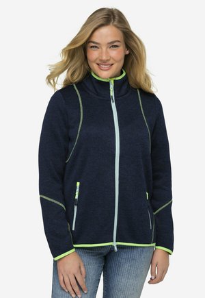 Giacca navy a zip con dettagli riflettenti di colore verde neon, tessuto testurizzato, colletto alto e due tasche con zip sul davanti.