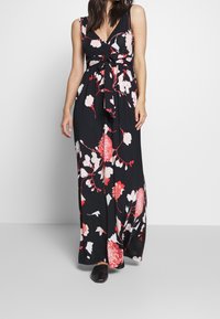 Maxi šaty z černé látky s velkými červenými a bílými květinovými vzory, s V-výstřihem a zúženým pasem. Hladká textura.