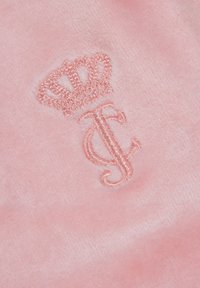 Rožinė pliušinė medžiaga su išsiuvinėta karūna ir inicialais "JC" atitinkančia rožinė siūle, kuri sukuria minkštą ir tekstūruotą paviršių.